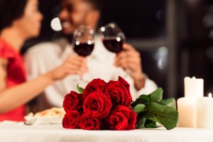 couple-toasting-with-wine-glasses-and-bouquet-of-roses-on-table